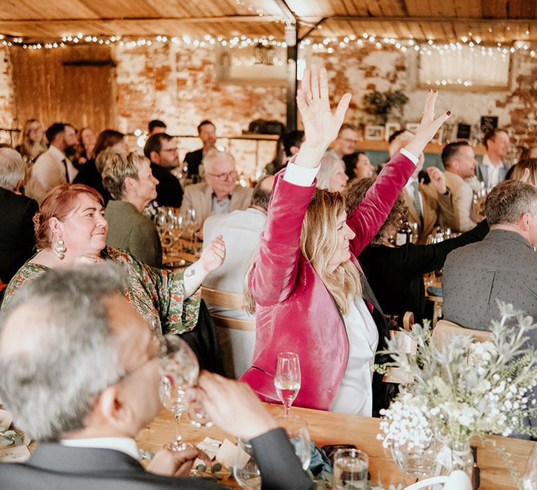 wedding guest in a pink velvet blazer waving her arms in the air at a rustic barn wedding reception 