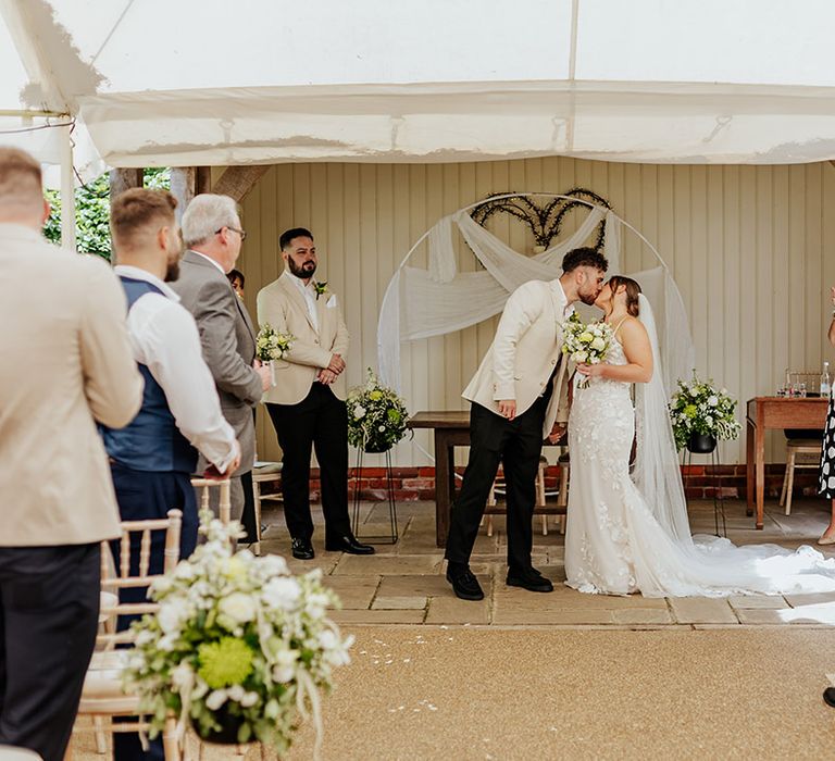 White wedding flower aisle decorations with the bride and groom sharing a kiss in front of moongate altar decor 