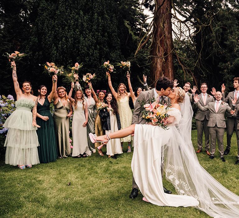 The bride and groom share an epic sweeping kiss as the wedding party watch and cheer on 