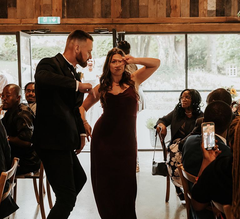 Bridesmaid in red bridesmaid dress entering reception with groom in black tuxedo entering reception dancing 