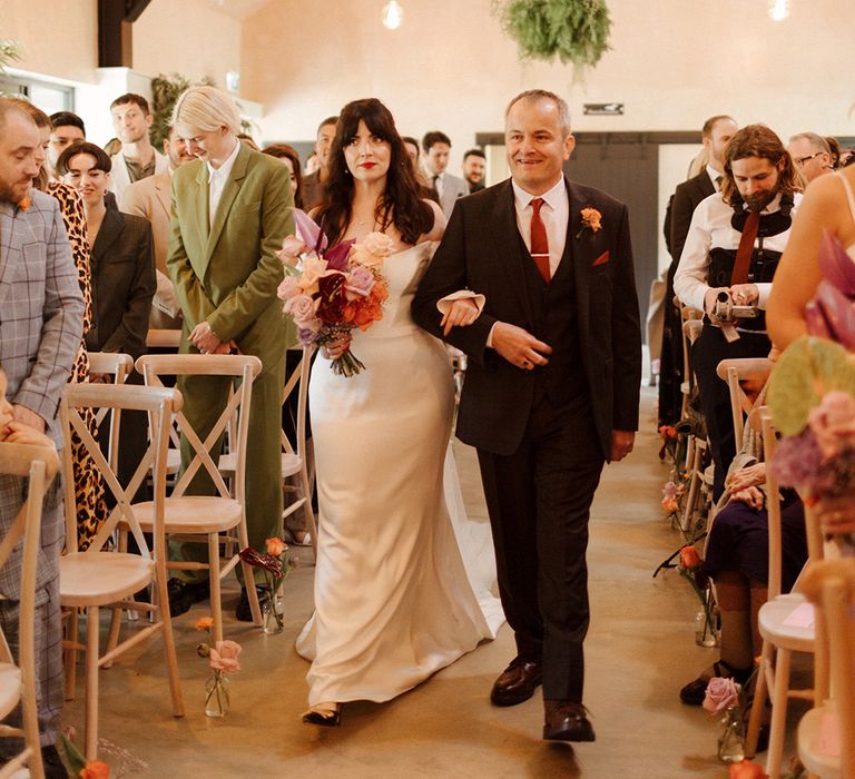 Bride in satin bespoke wedding dress walking down the aisle with father of the bride 