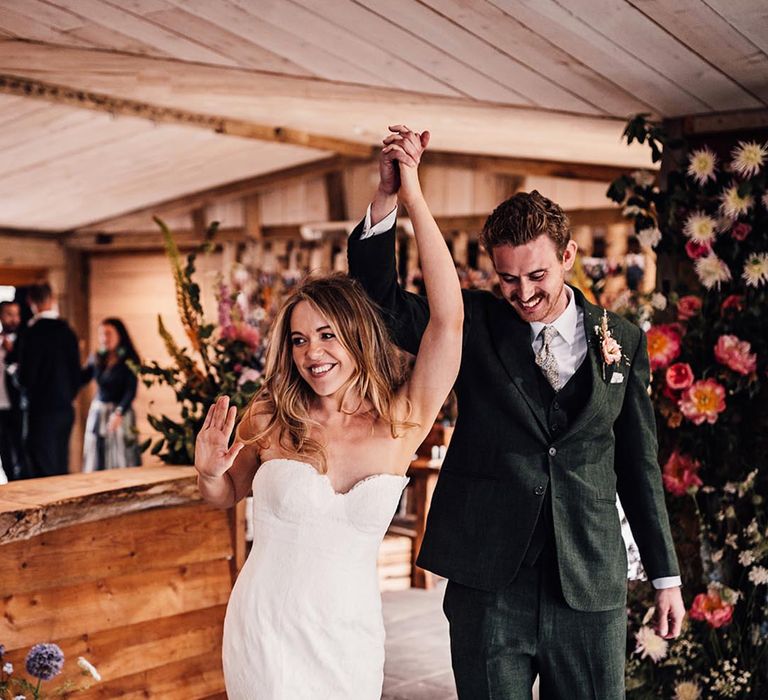 The bride and groom raise their joined hands in the air as they enter their wedding reception together 