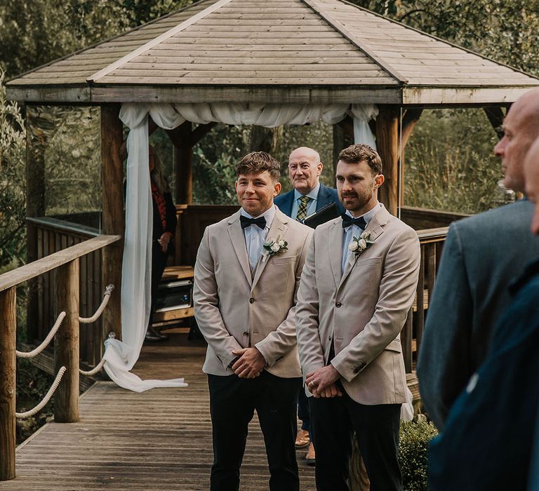 The groom and best man stand together as the bride walks down the aisle 