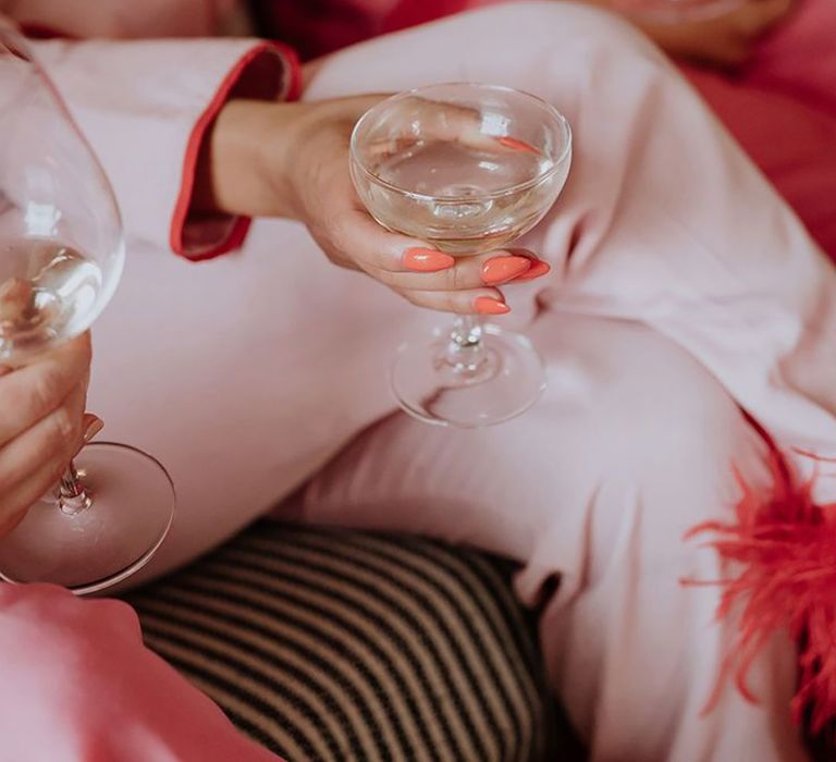 Bride with long almond pointed wedding nails in a hot coral pink shade holding champagne coupe 