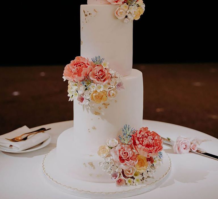 Three tier traditional tall wedding cake decorated with colourful pastel wedding flowers for minimalist style 