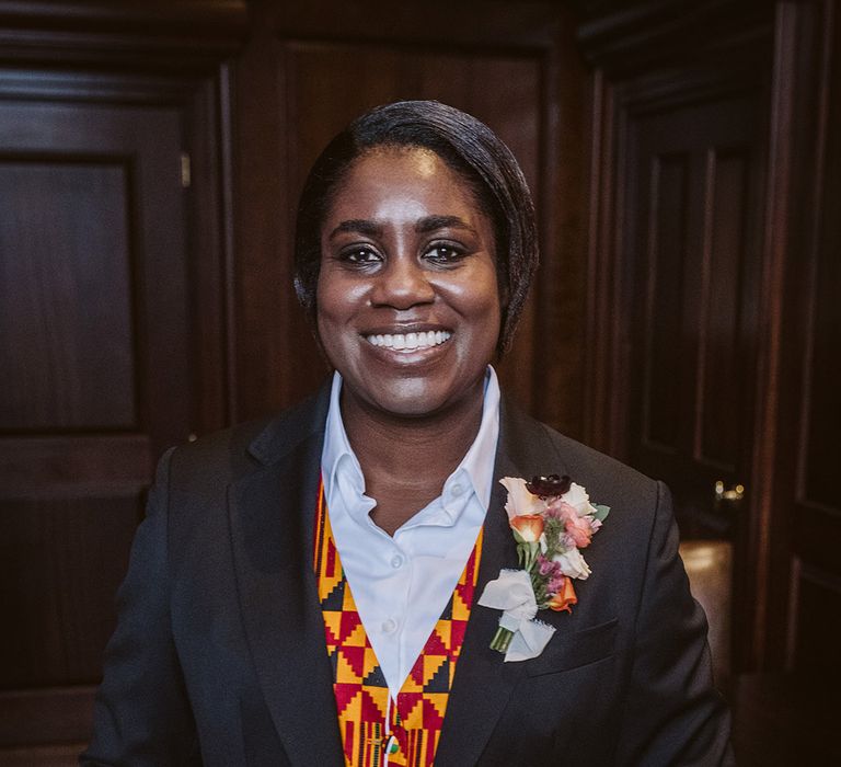 Bride in black suit jacket with patterned Ghanian waistcoat with floral buttonhole at multicultural lesbian LGBTQI+ wedding 