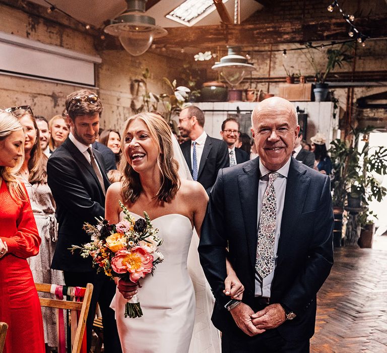 Bride wearing strapless wedding dress with the father of the bride walking down the aisle 