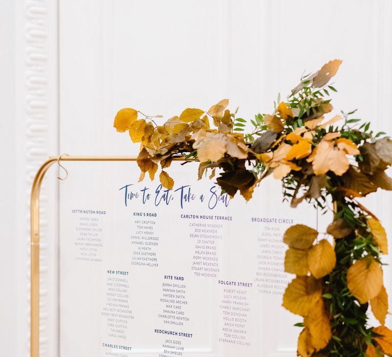 Acrylic seating chart on a gold frame with autumn flowers decorating 