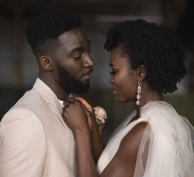 Black bride with short curly hair and smokey eye makeup adjusting her grooms tie 