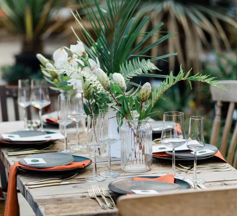 Rustic jungle wedding decor with orange napkins, jungle centrepiece and gold dinnerware