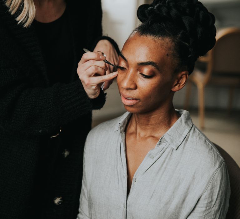 A bride sits having her make up done. Her hair is in twists and arranged in a bun on top of her head.