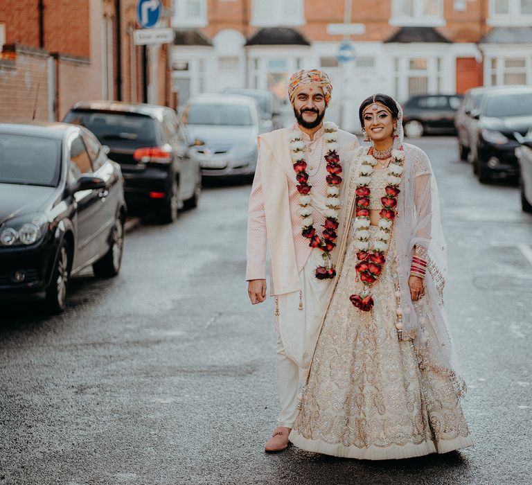 Bride & groom stand together outdoors wearing rose Lei's 