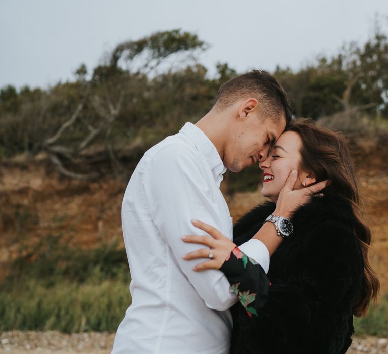 Groom-to-be in a white shirt leaning on his bride-to-be's forehead holding her face