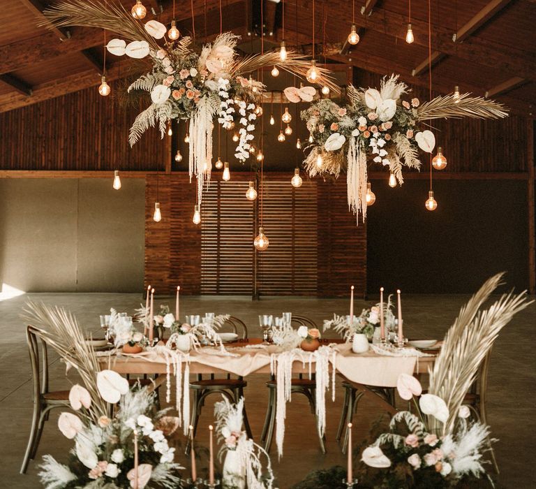 Barn wedding venue decorated with an intimate tablescape full of boho wedding flowers, taper candles, natural linens and festoon light installation 