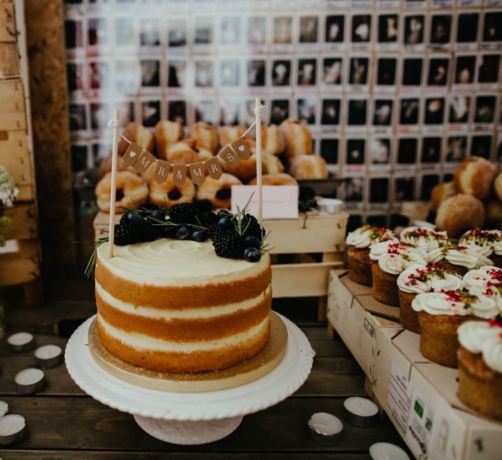 Small naked wedding cake with buttercream icing, topped with blueberries, blackberries and rosemary and a Mr & Mrs bunting cake topper.