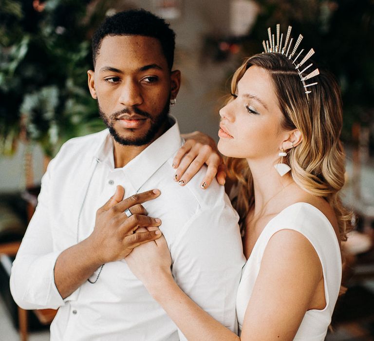 Groom in a white open shirt holding his brides hand with stylish nail art, bridal crown and long wavy hair 