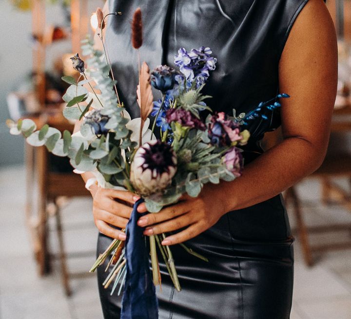 Bridesmaid in a high neck leather dress holding a moody dark wedding flowers bouquet 