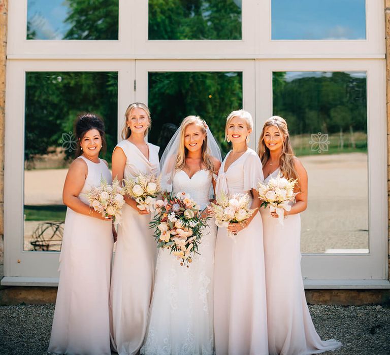 Peach wedding inspiration - bridal party stood outside country barn wearing pink bridesmaid dresses and bride wearing white lace bridal gown