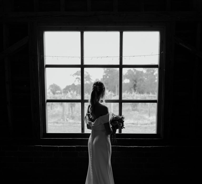 Bride stands in front of window with her dress fanned out behind her