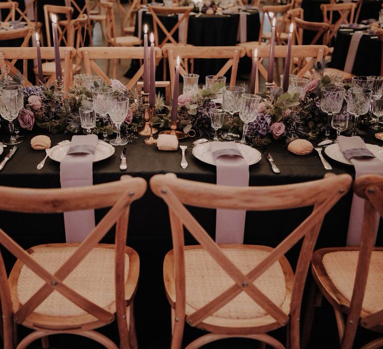 Purple floral table centrepieces with thistles, hydrangeas and roses, plus wooden chairs, purple napkins and cut crystal glassware