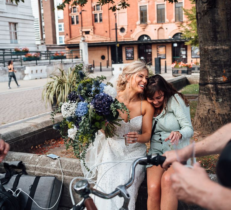 Bride sits with wedding guest and holds champagne after wedding ceremony