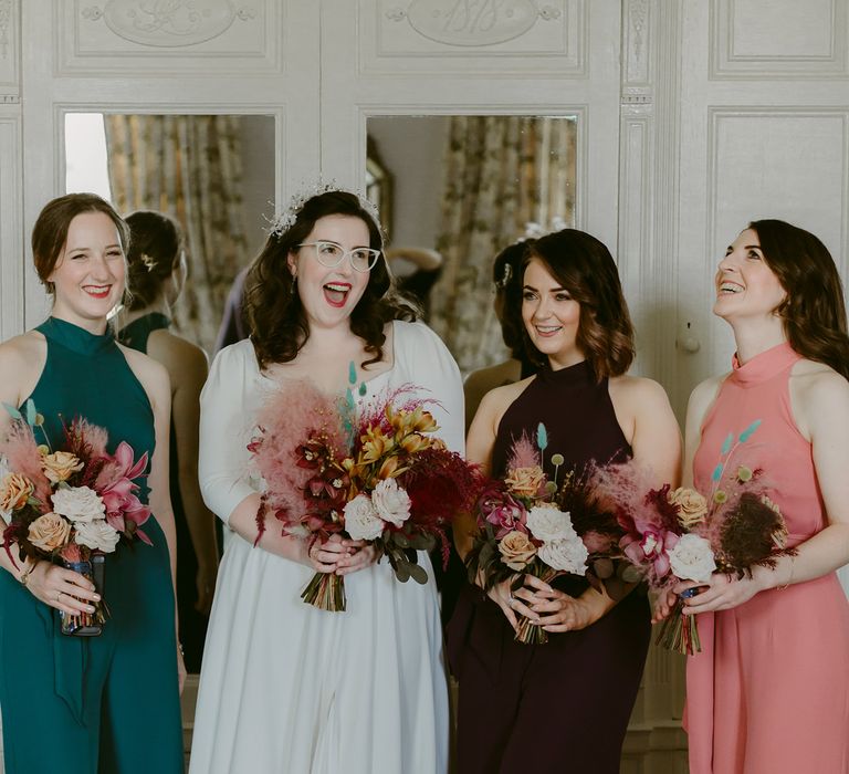 Bride in white Rime Arodaky dress and bridesmaids in different coloured Rewritten bridesmaids dresses hold pink and white rose and pampas grass bouquets