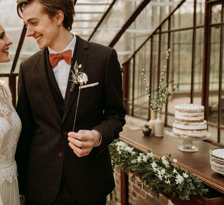 Bride and groom holding sparklers at glasshouse wedding with semi-naked wedding cake in the background