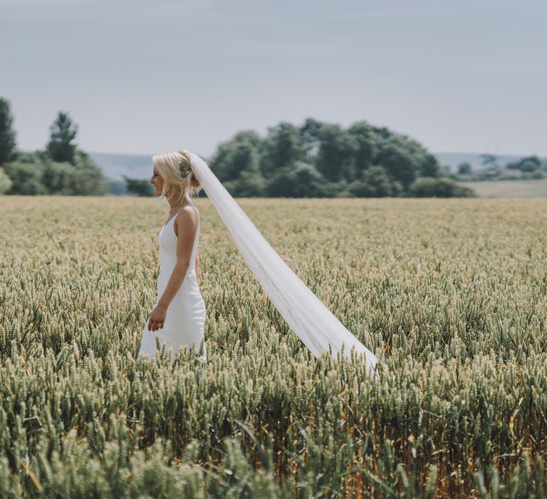 Bride walks through fields with her veil blowing behind her