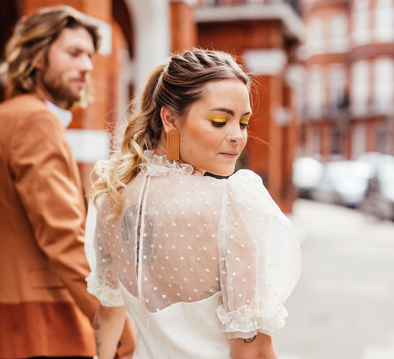 Stylish bride in a polka dot wedding dress looking over her shoulder with retro earrings and yellow wedding makeup 