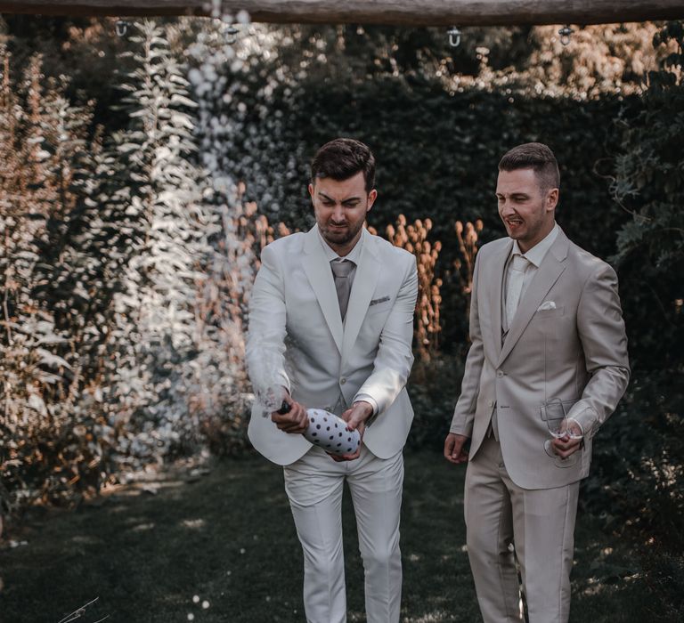 Grooms pop the champagne in light grey wedding suits