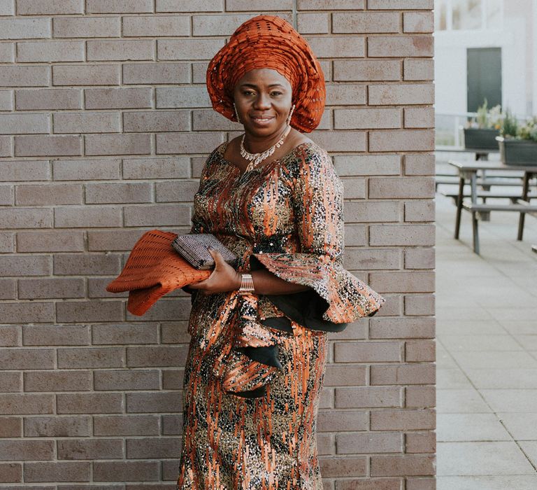 Smiling wedding guest in long orange and black printed dress with wide sleeves, orange headscarf and silver jewellery 