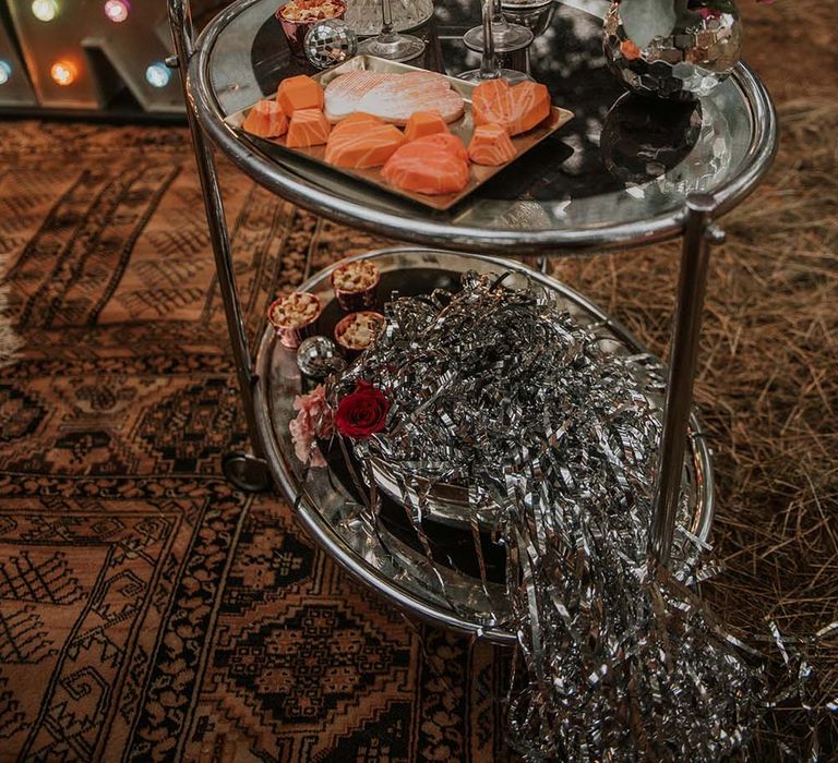 Silver bar table with silver streamers, orange hearts, crystal cut glassware and tropical floral details at festival themed wedding