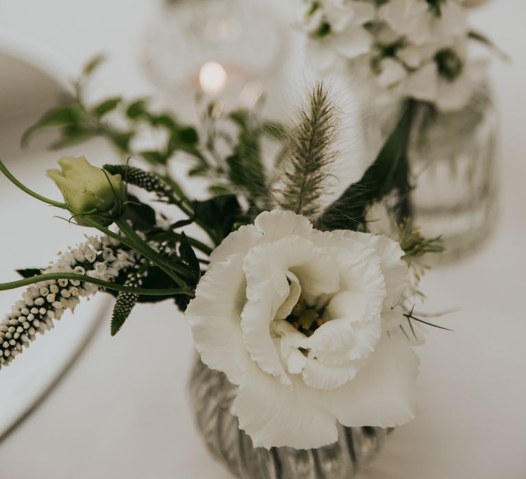 Small white floral arrangement with green foliage lines the table for reception dinner