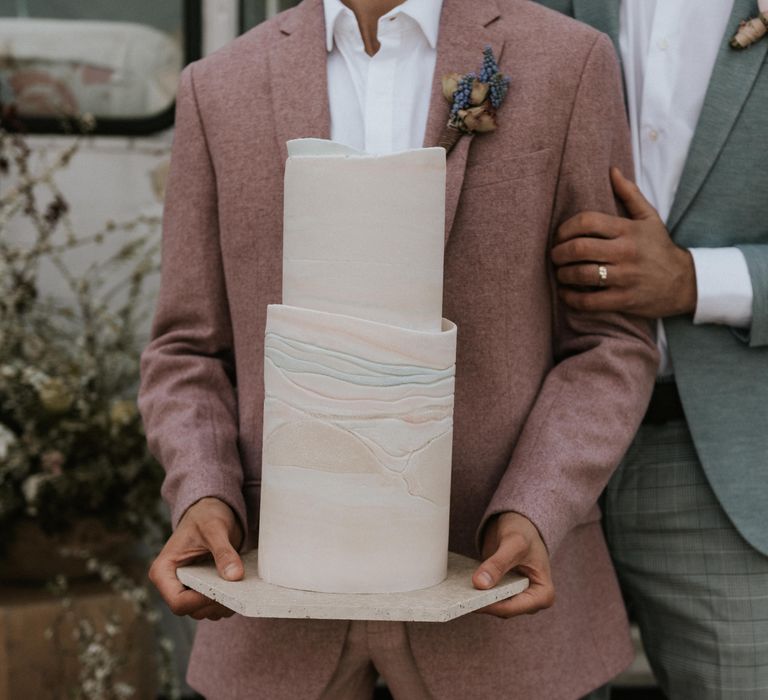 Grooms wears pastel suits whilst holding modern wedding cake with pastel colouring