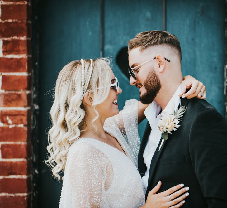 Stylish bride and groom in a sparkly wedding dress and white cat eye, and a black suit and aviator sunglasses