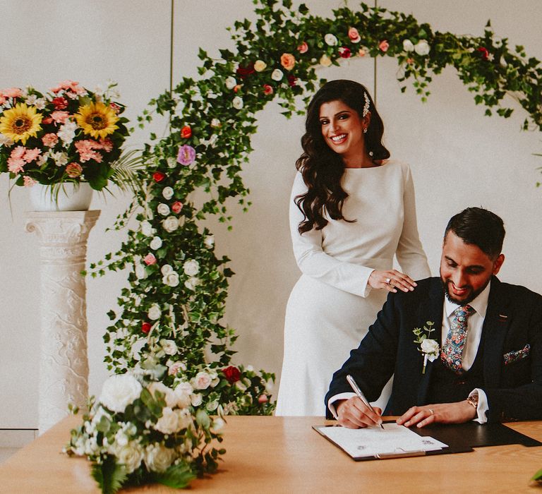 Bride and groom signing the register at Brent Civic Centre wedding venue with a foliage and sunflower moon gate 