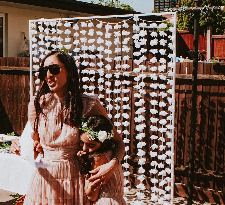 Garden party reception with bridesmaid and flower girl giving a speech in front of a flower wall 