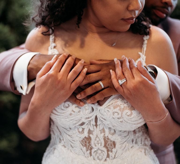 Bride wears lace strappy gown as groom wraps his arms around her and she holds onto his hands