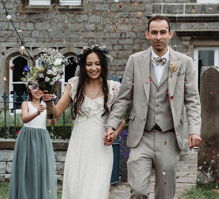 Bride & groom walk hand in hand together as confetti is thrown around them on their wedding day