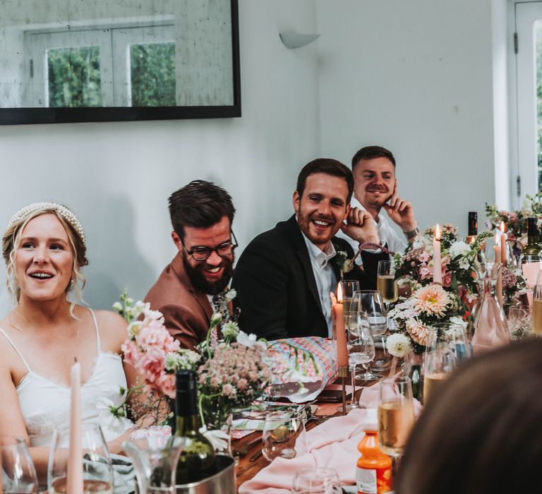 Wedding guests gather around table for wedding reception meal as they laugh and listen to speeches 