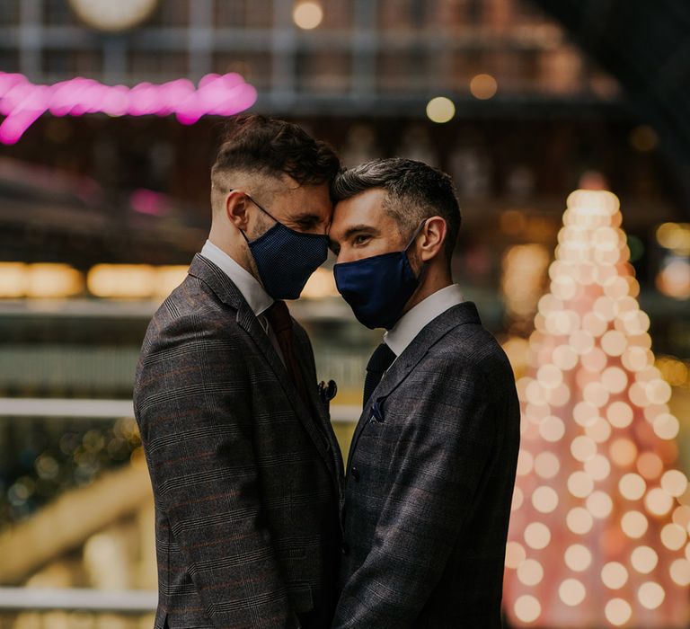 Grooms touch their foreheads against one another as they wear face masks in train station