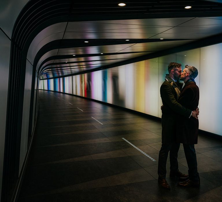 Grooms embrace one another in walkway before wedding ceremony