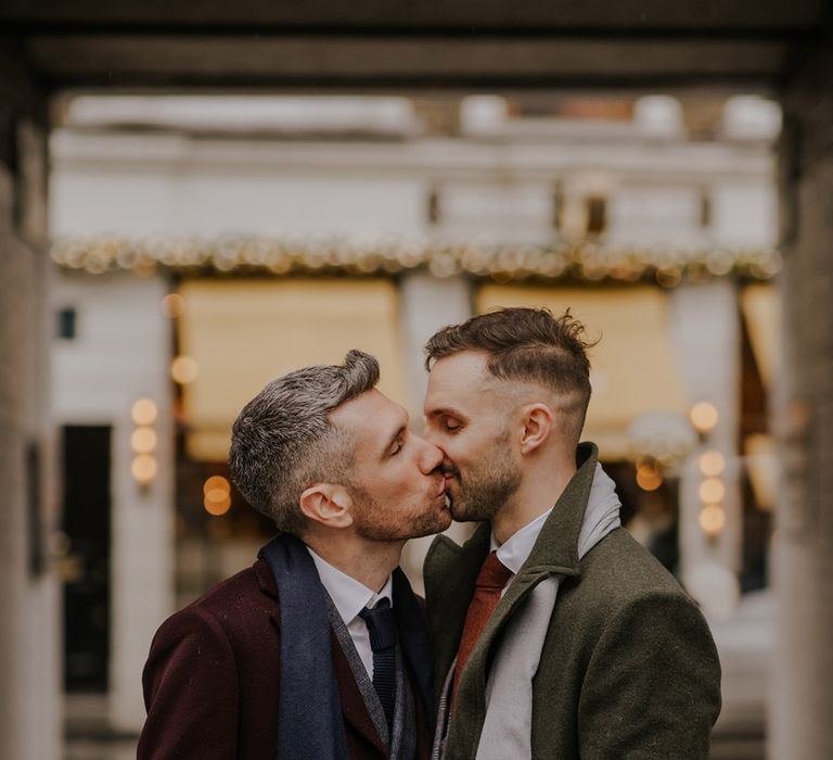 Grooms kiss outdoors on their wedding day in London as they wear stylish coats and scarves 