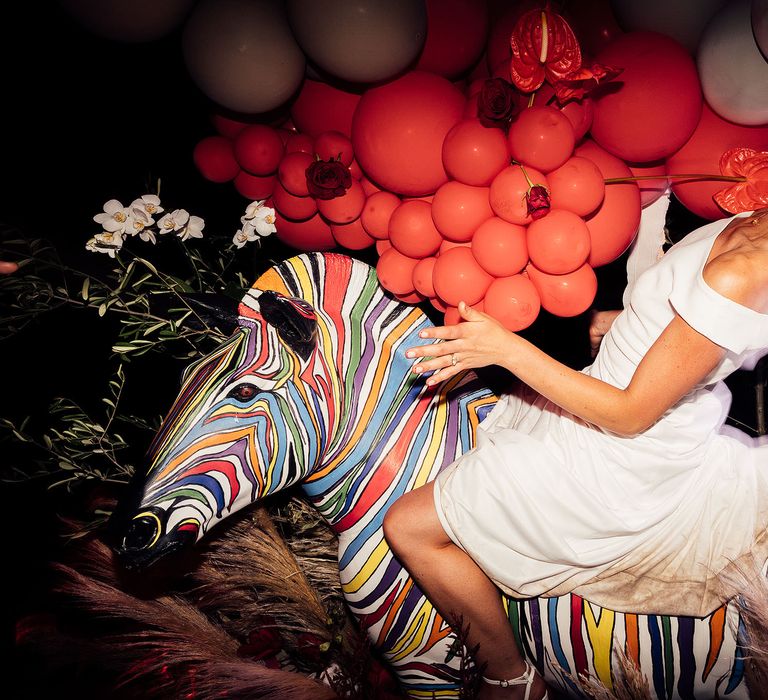 Bride on colourful zebra with dried flower installation with balloons and neon sign