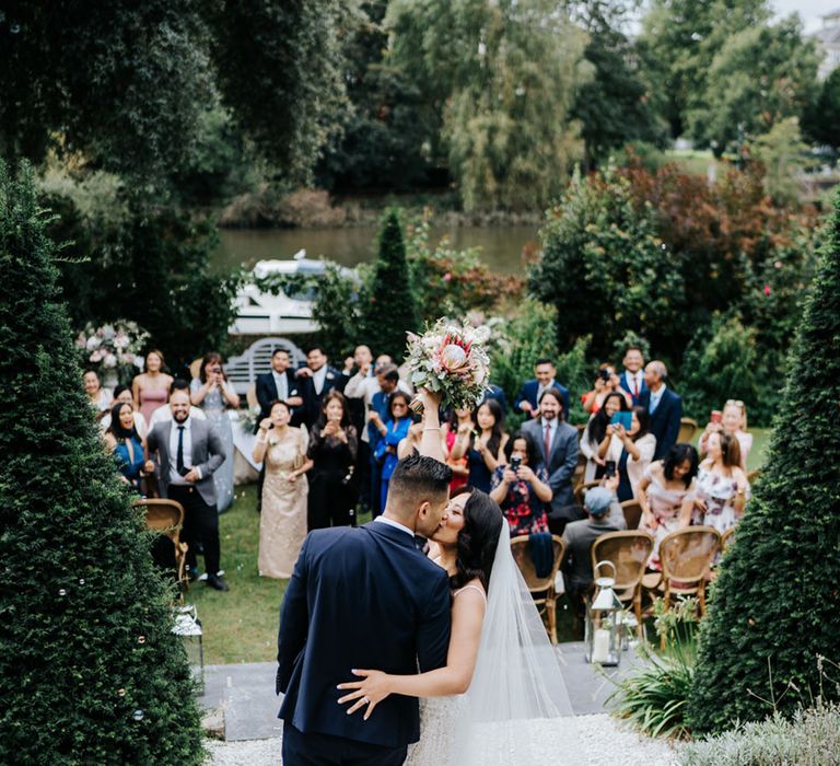 South Asian Groom & Bride kiss as their wedding party cheer at Bingham Riverhouse 