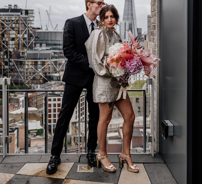 Bride and Groom on balcony with London skylights in the background, Bride holding a beautiful pastel colour palette of hydrangea with a pop of colour 