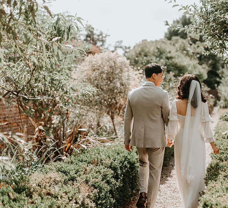 Bride & groom walk hand in hand on their wedding day through the Secret Garden venue