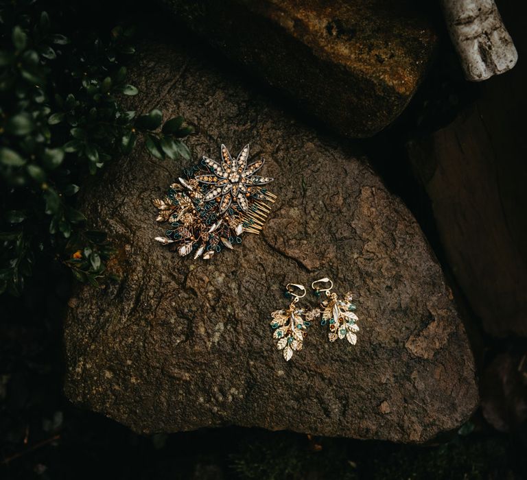 Bejewelled hair comb and leaf earrings laid on rock outside at farm wedding