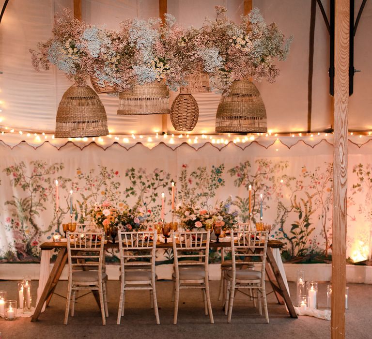 Wooden table and chairs with boho rustic decor in modern marquee tent with embroidered sides for wedding reception 