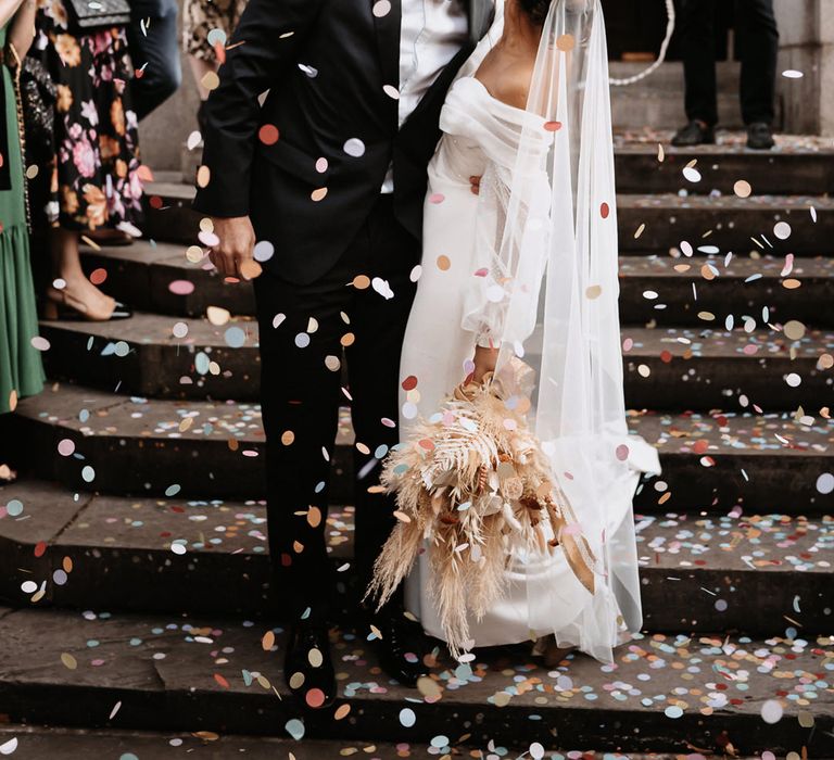 Confetti moment on the steps of Chelsea Town hall with bride in a strapless wedding dress and groom in a tuxedo 